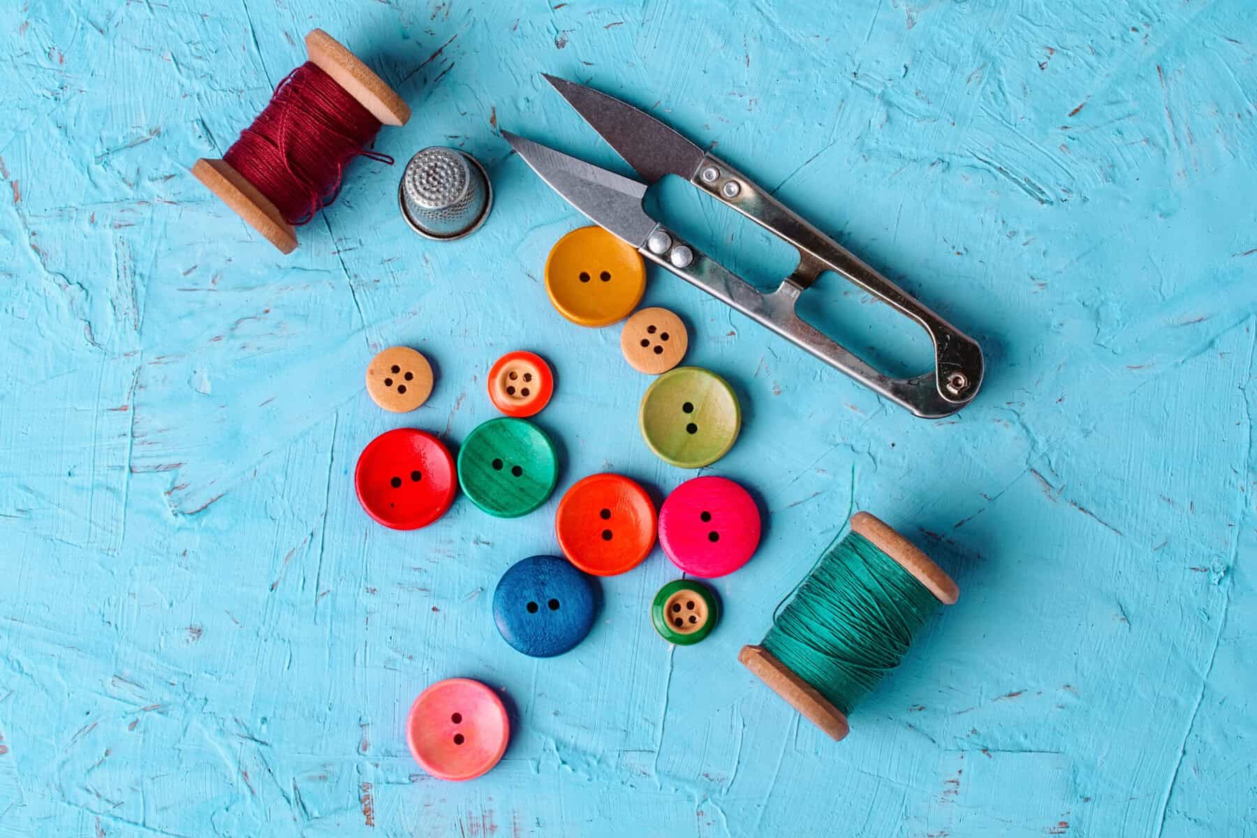 robin's egg blue table with colorful buttons, thread, thimble, and snips on it.
